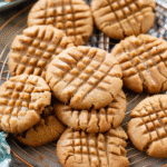 A batch of soft peanut butter cookies with crisscross fork marks, cooling on a wire rack.