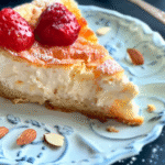 A slice of low-carb Greek yogurt almond cake topped with fresh strawberries, served on a decorative blue plate with scattered almond slices.