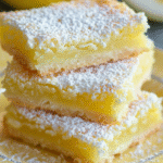 Close-up of three stacked lemon curd bars dusted with powdered sugar on a decorative plate.