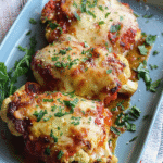 Baked cauliflower steaks topped with marinara sauce and melted cheese, garnished with chopped parsley on a blue serving dish.